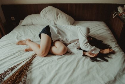 Женщина лежит на кровати, закрыв лицо руками.